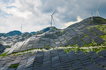 Wind turbines and solar panels generating renewable energy on mountain background.