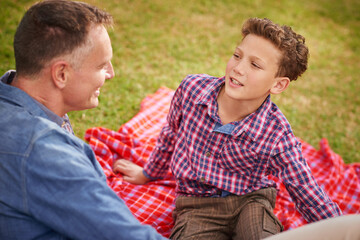 Talking, father and son in park, picnic and bonding together with care, trust or summer break. Family, outdoor or dad with kid, conversation or parent with child, love or vacation with story or relax