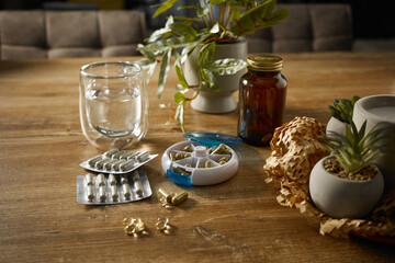 Daily medication setup on a wooden table with water and plants in the background during daylight hours