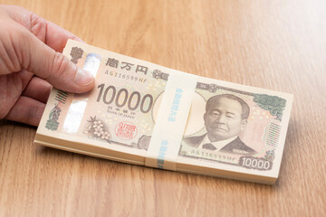 一万円札の札束を手に持つ日本円の高額資金イメージ