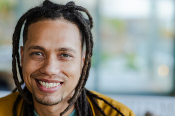 African American man smiling broadly at camera in lounge wearing mustard jacket over green shirt