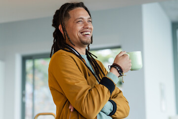 African American man smiling while looking out in lounge with bracelets holding light green mug