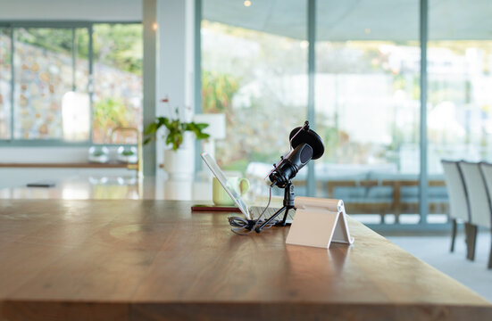 USB condenser microphone is sitting on tripod by glass windows with laptop and green mug