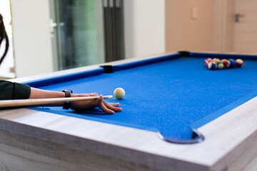 Right hand aligning cue stick with white ball on blue felt pool table near glass door