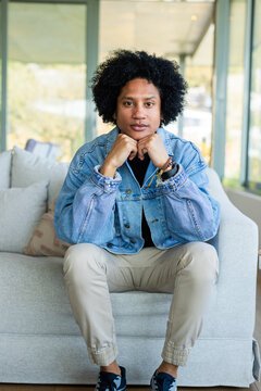African American man leaning forward on gray sofa beside glass panels in living room