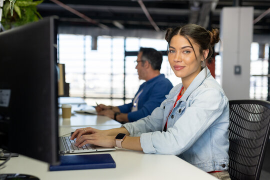 Diverse coworkers typing on laptop while using desktop monitor at desk with coffee cup, copy space