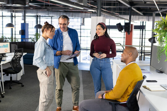 Diverse coworkers discussing project standing and sitting in modern office with monitor and tablet