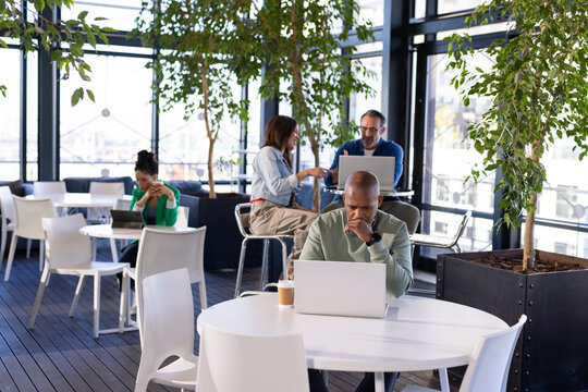 African American man working on laptop with coffee cup at shared workspace overlooking waterfront