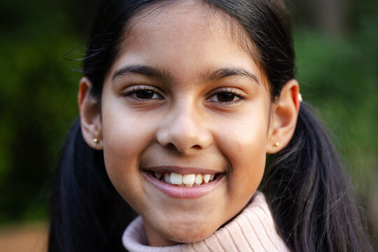 Indian Asian child girl smiling while posing in garden wearing pink turtleneck sweater