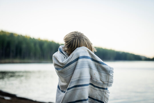 A young boy dries his hair in a towel at edge of lake