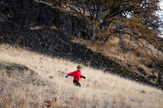 A smiling young boy runs down a tan field of grass.