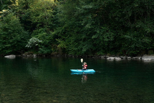 A young boy paddles a small kayak on a clear, calm river