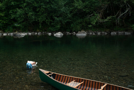 A young boy crouches in shallow river with snorkel mask and canoe