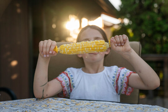A young girl eats corn on the cob backlit by sunset