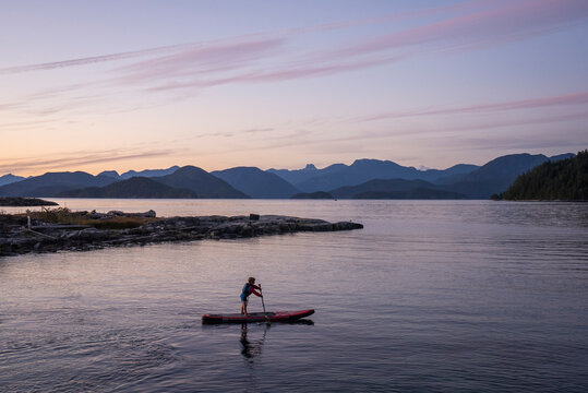 A young boy paddle boards at dusk among mountains