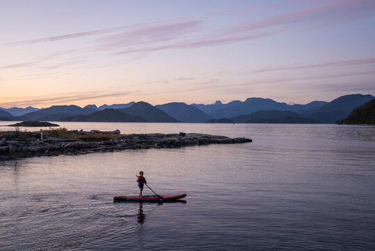 A young boy paddle boards at dusk among mountains