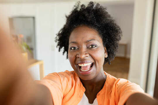 African American woman wearing orange shirt taking selfie at home with smartphone