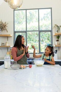 African American mother clapping while daughter whisking batter at kitchen countertop