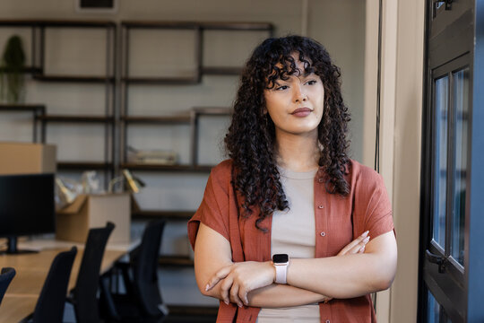 African American woman standing near window at workspace viewing monitors and checking smartwatch