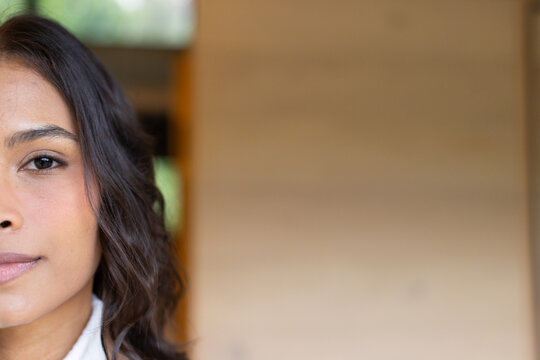 Close-up capturing left side of woman's face with dark hair against panel wall and green foliage