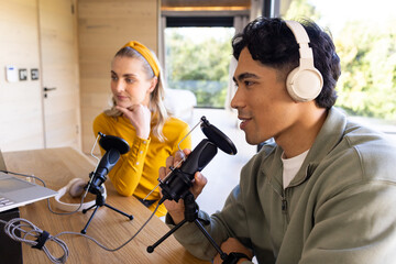 Diverse cohosts recording podcast episode in modern home studio using microphones and laptop
