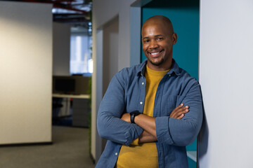 African American man leaning on wall in office corridor wearing smartwatch beside computer monitor