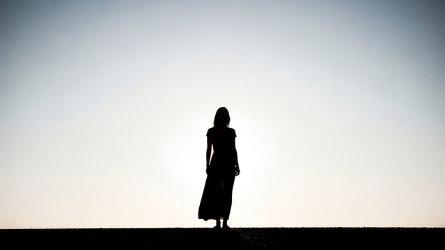 Woman standing silhouetted against the bright sky at sunset for International Women's Day - Powered by Adobe