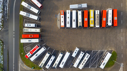 Aerial view of a bus depot with parked vehicles, marked parking spaces, curved layout of the yard and surrounding access roads © Adam