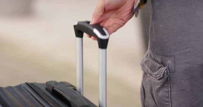 Right hand pressing button on suitcase at terminal entrance extending telescopic handle for pulling