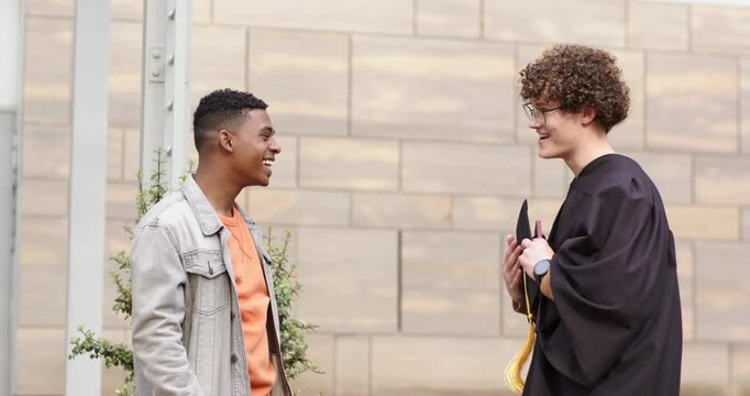 Diverse male friends offering cap holding diploma showing phone in wallet-style case in courtyard