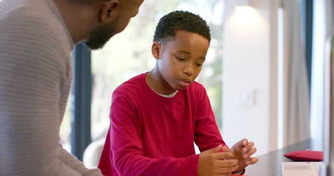 Placing notebook and red device, African American father and son studying object at kitchen island