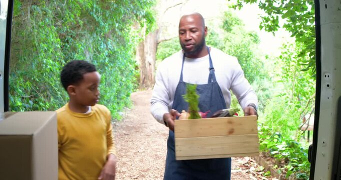 With van doors open father and son loading vegetables into van on rural lane, bumping fists
