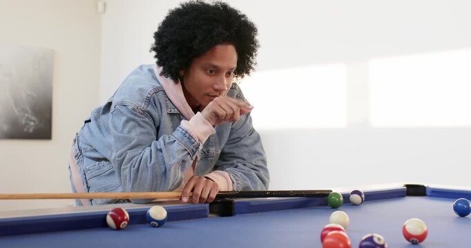 Mid adult man leaning over pool table holding cue pointing target planning shot in recreation room