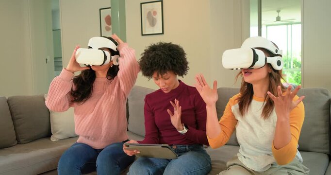 Diverse female friends putting on VR headsets, using tablet to launch app, gesturing in living room