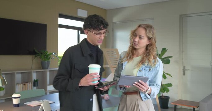 Diverse coworkers tapping data on tablet at office table with colleague entering to join meeting
