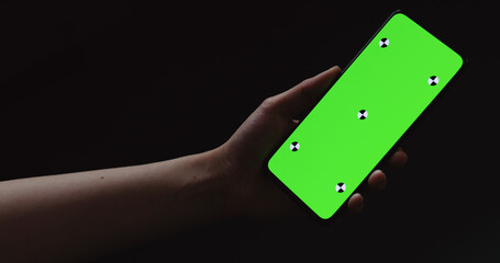 young woman sitting at the black table near window and holding smartphone with horizontal green screen