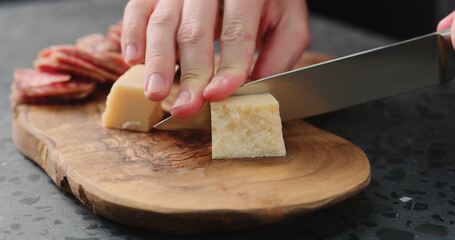 man slicing parmesan hard cheese on olive wood board