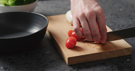 man slicing cherry tomatoes on oak board