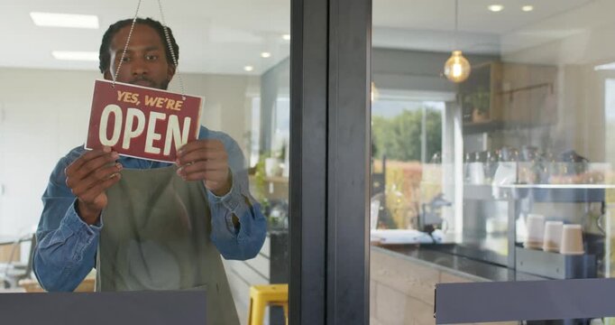 African American male barista opening coffee shop unhooking sign flipping to open peering outside