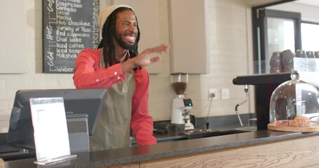 African American male barista responding to wave grabbing cups sliding tray to customer at cafe