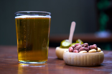 A glass of beer with snacks on a wooden table.