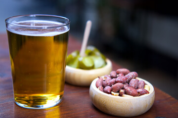 A glass of beer with snacks on a wooden table.