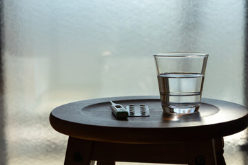 窓際に置かれた体温計と薬とコップに入った水