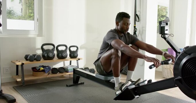 Mid-adult African American man pressing heels, pulling handle on rower in home gym for strength