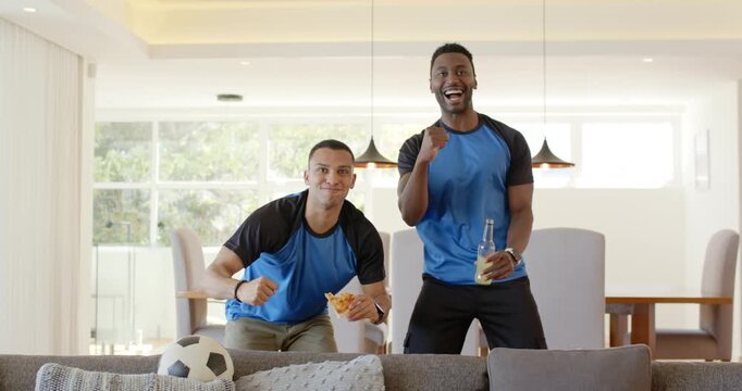 Diverse male friends at home reacting to game escalating pumping fists shaking hands holding pizza