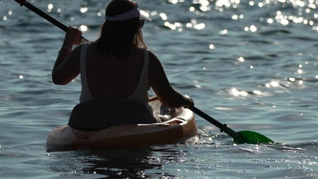 Kayaking paddling silhouette woman enjoying leisure time on sparkling ocean water