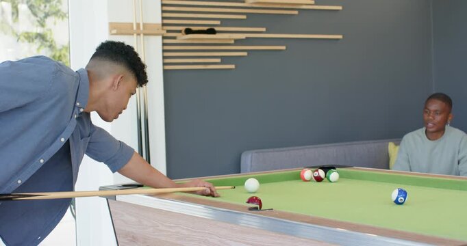 Man approaching pool table and striking ball with cue stick then shaking friend's hand in lounge