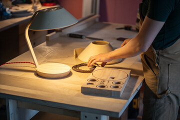 Man carpenter manufacturing wooden lamp with unique design in carpentry workshop at table, process of choosing right wire, small woodshop business and production, handmade items for home and living.