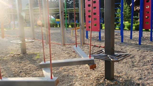 Wooden beams hang on red ropes while low summer sun throws flare. Balance path invites training with soft gravel surface reducing slips