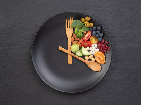 Intermittent fasting concept, spoon and fork on a black plate with food looking like a clock